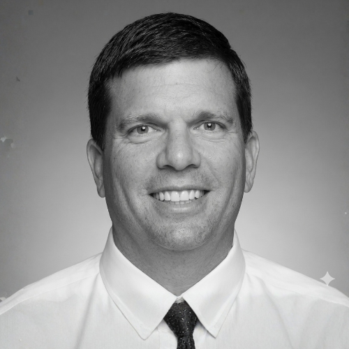 A headshot of a person with short dark hair, wearing a white collared shirt, smiling at the camera against a white door.
