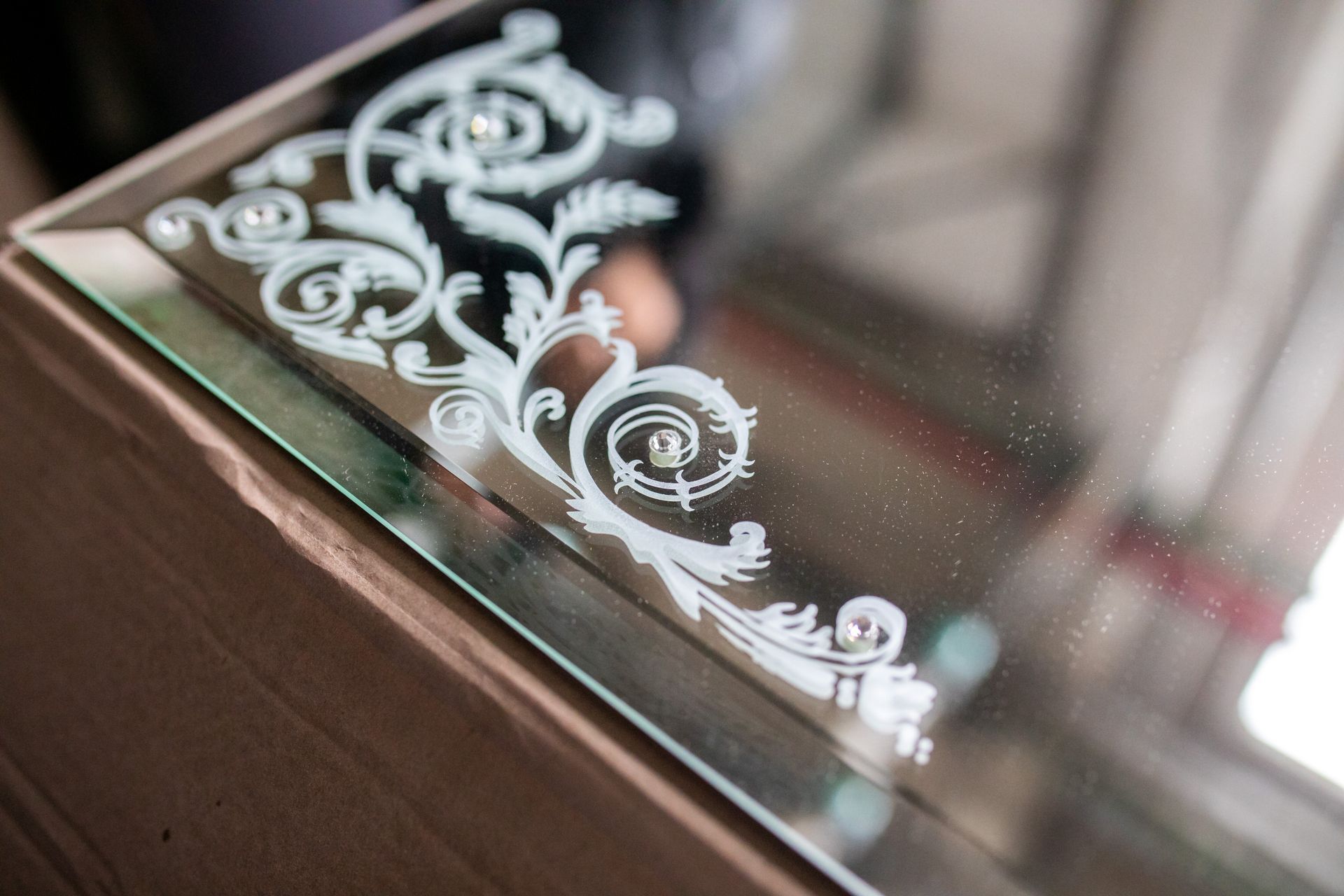 Decorative etched mirror corner with white floral scrollwork on a wooden table