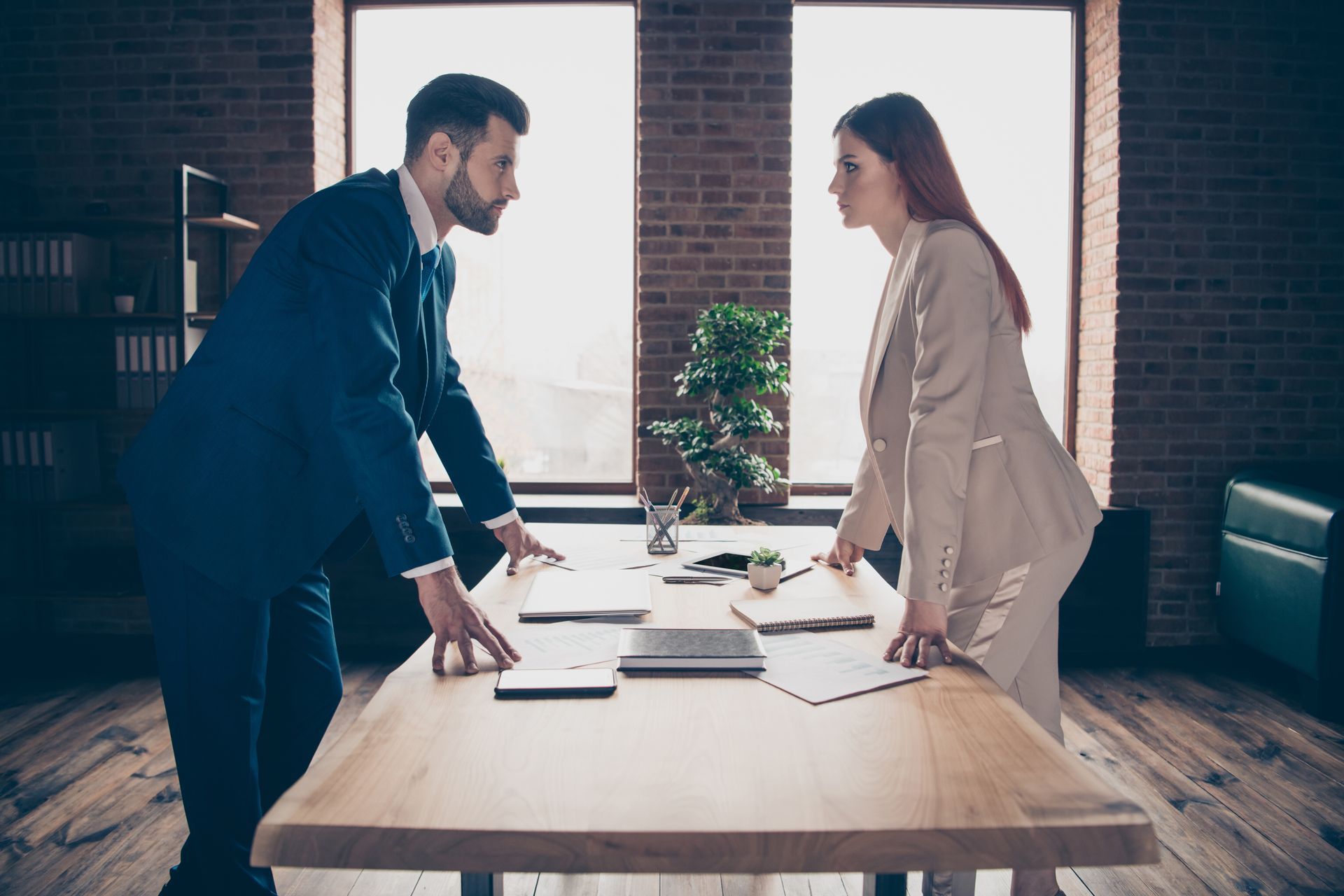 A man and woman are engaged in a discussion in an office setting, with papers scattered on the desk
