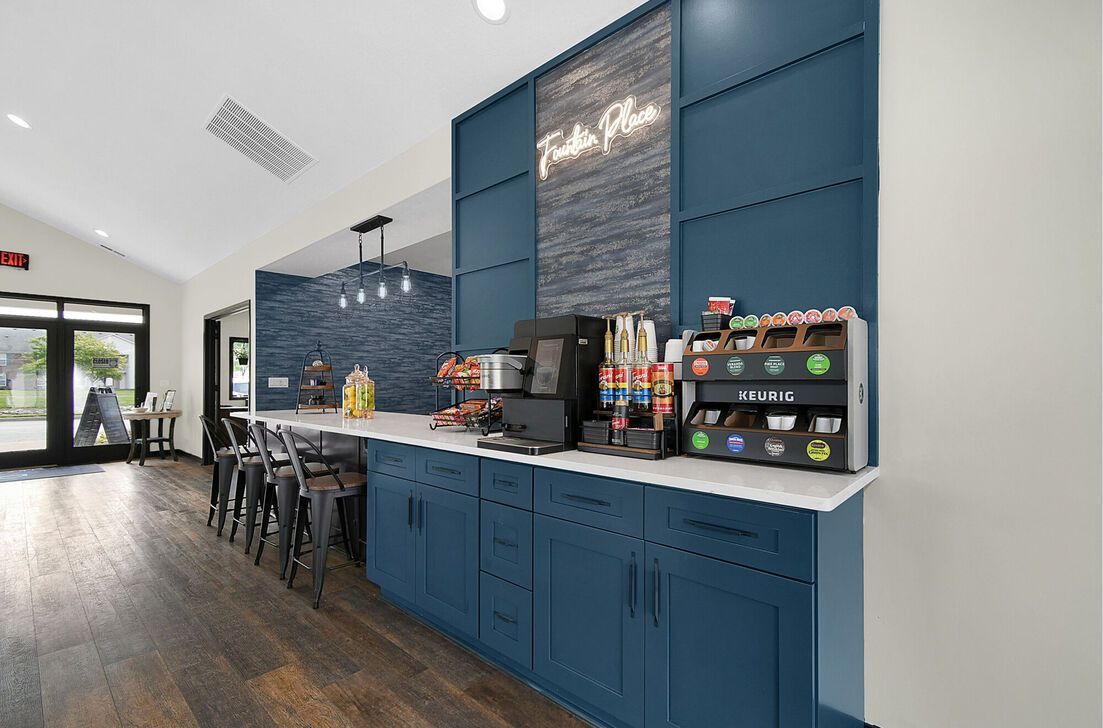 Modern café counter with blue cabinetry, coffee machines, and stools in a bright room