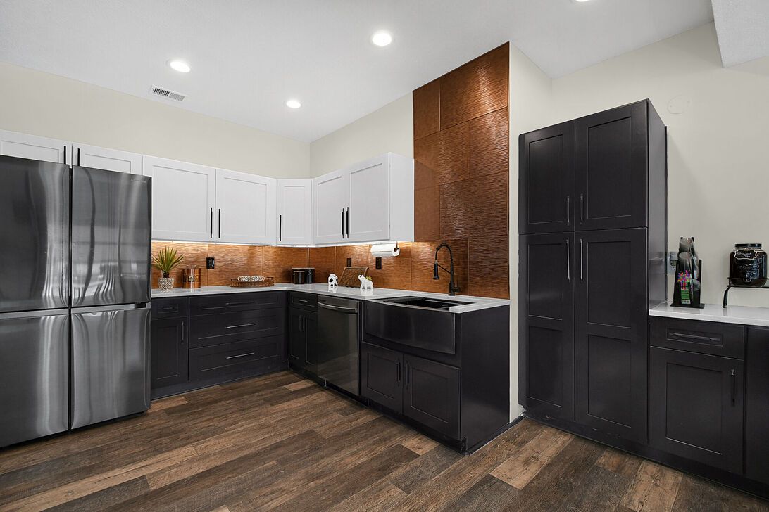 Modern kitchen with black and stainless steel appliances, white cabinets, wood flooring, and copper backsplash lighting