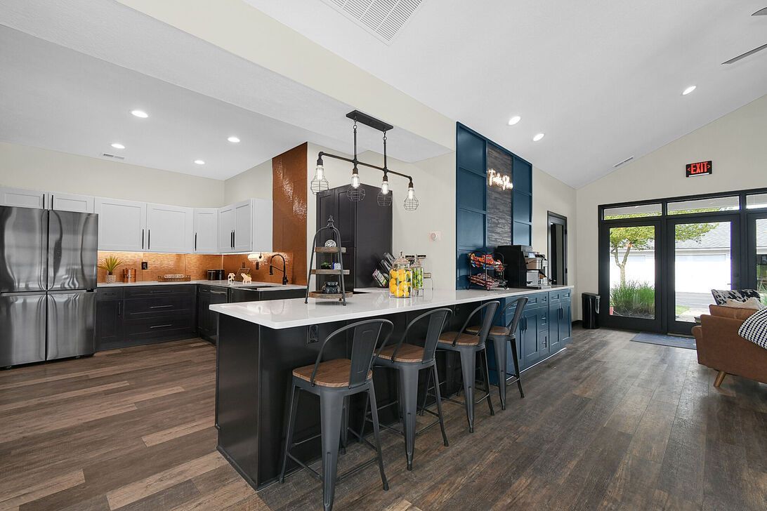 Modern kitchen with dark island, black barstools, white cabinets, and wood floors in an open interior