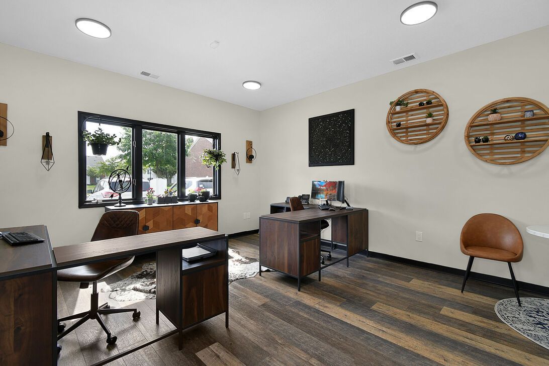 Modern office with desk, chairs, striped rug, wall art, and large windows letting in natural light