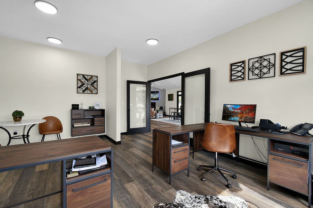 Modern home office with two desks, computer monitors, dark wood floors, and French doors to another room