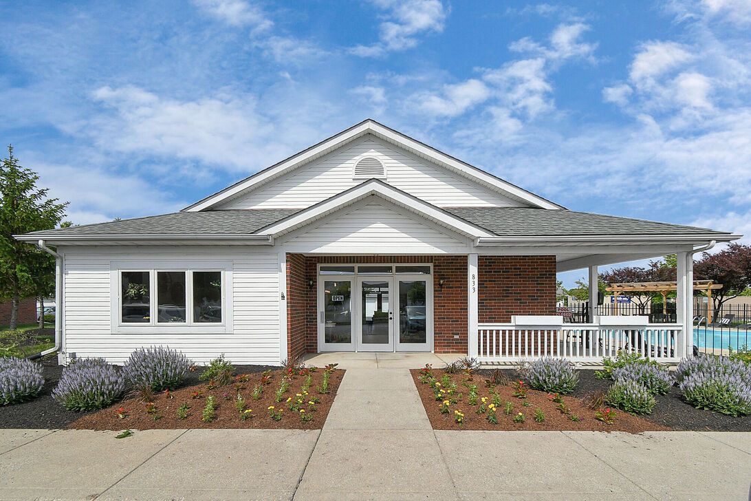 White single-story house with a front porch, double doors, and landscaped flower beds under a blue sky