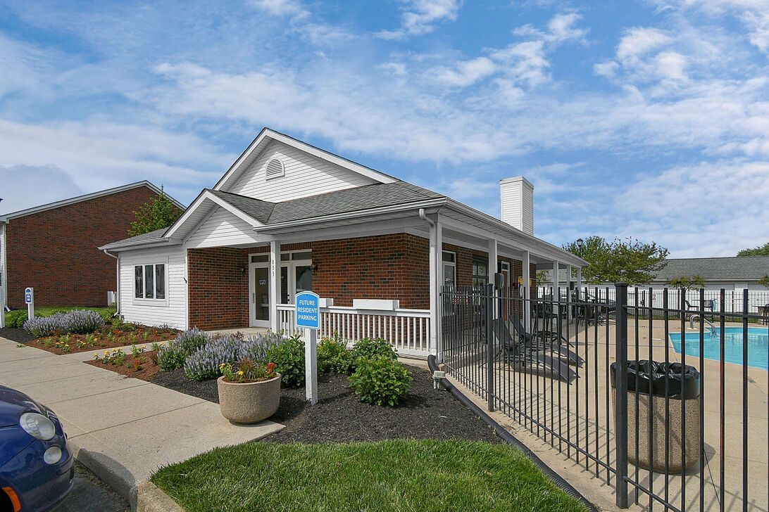 White house with porch beside a fenced swimming pool under a blue sky