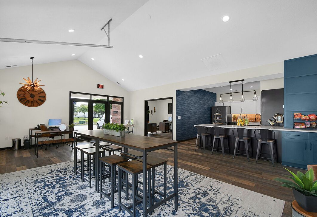 Modern cafe with high tables, blue walls, patterned rug, and seating near large windows