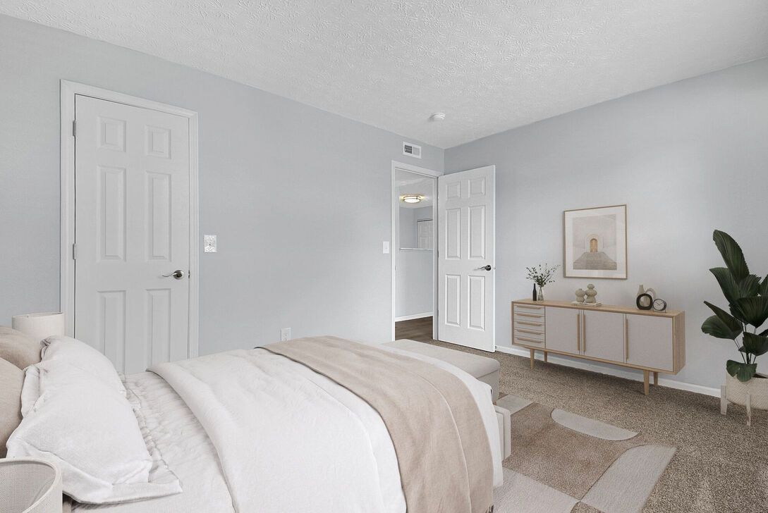 Bright bedroom with a made bed, light gray walls, white doors, and a console table with decor.
