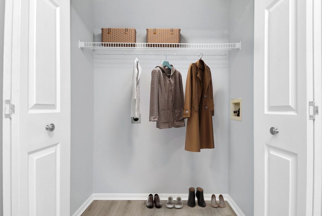 Entryway closet with white doors, hanging coats, shelves with baskets, and shoes on the floor