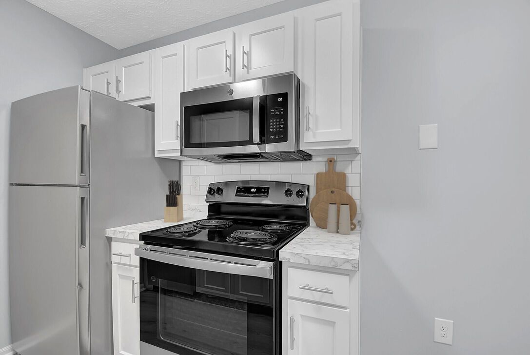 Small white kitchen with stainless steel stove, microwave, and refrigerator, plus white cabinets.