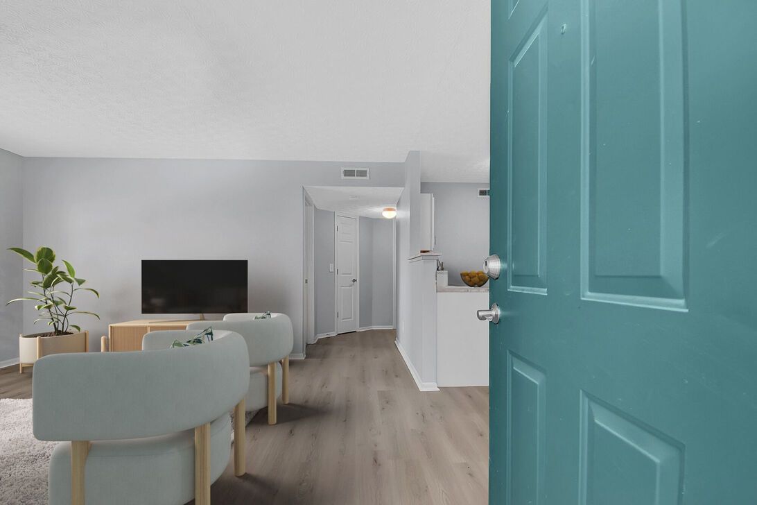 Bright living room with teal door, gray chairs, TV, plant, and hallway view