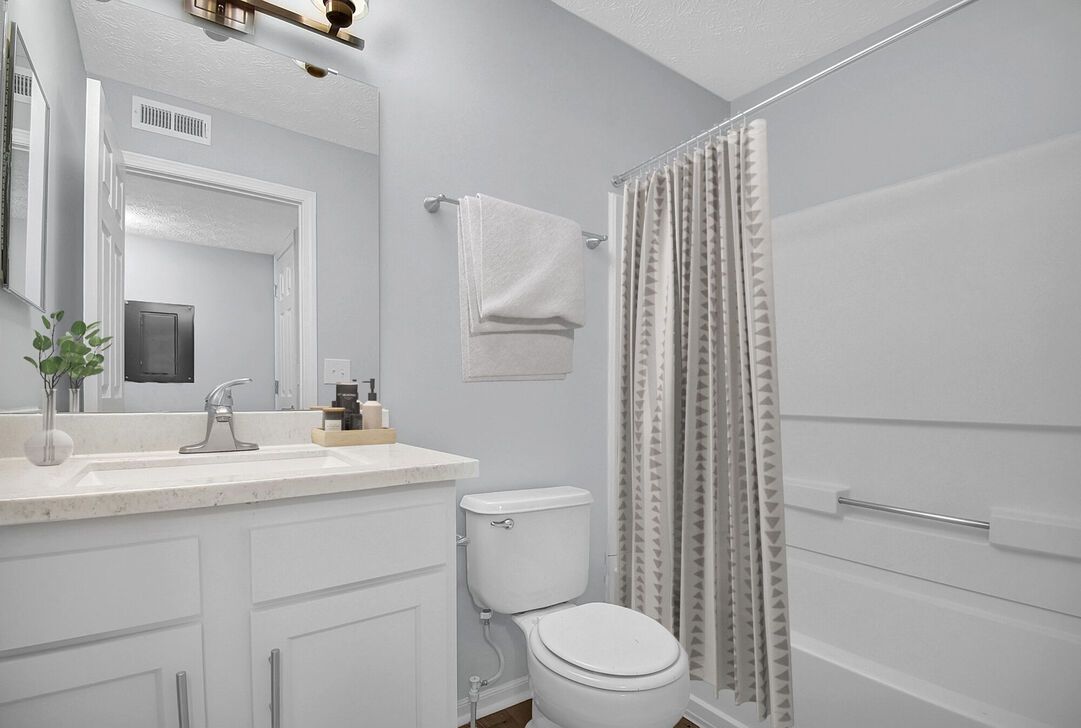 Bright white bathroom with vanity, toilet, towel rack, and shower curtain.