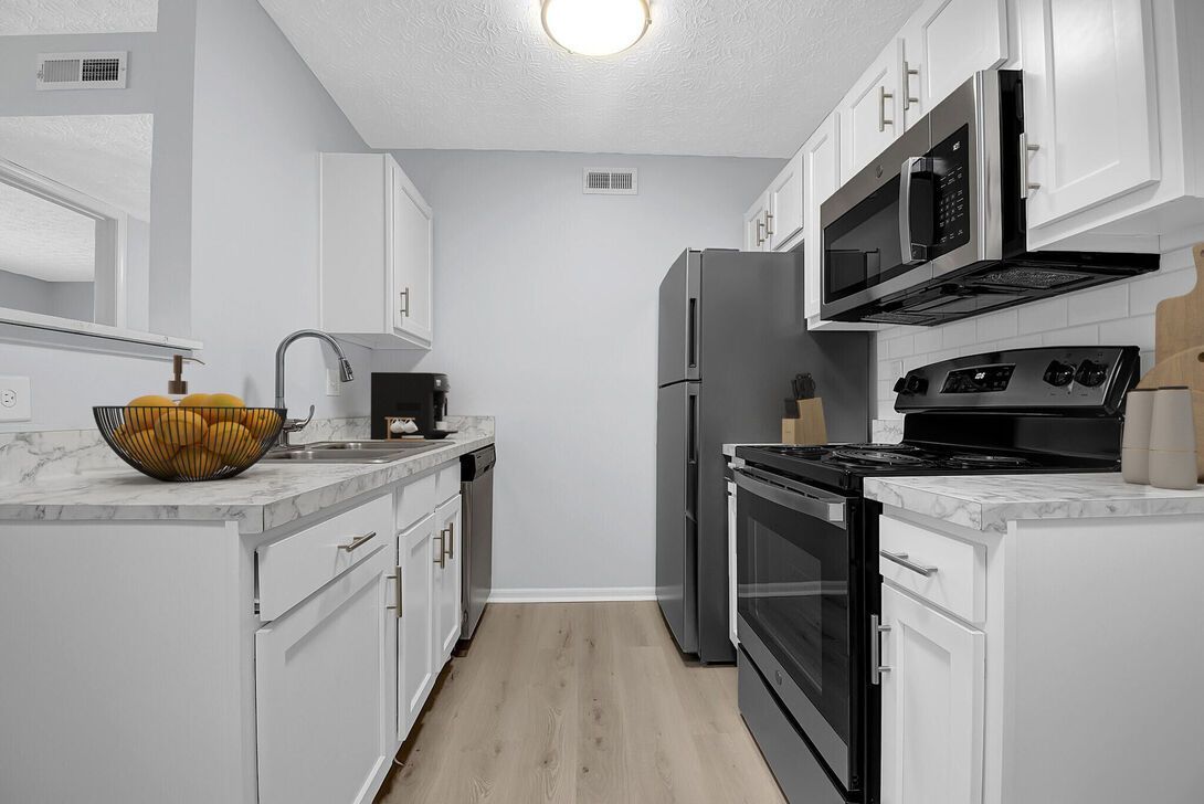 Modern white kitchen with stainless steel appliances, white cabinets, and a bowl of fruit on the counter