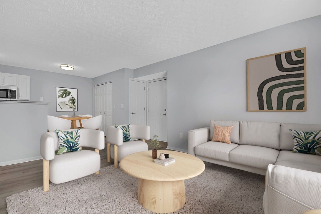 Bright modern living room with beige sofa, white chairs, round wood coffee table, and abstract wall art.