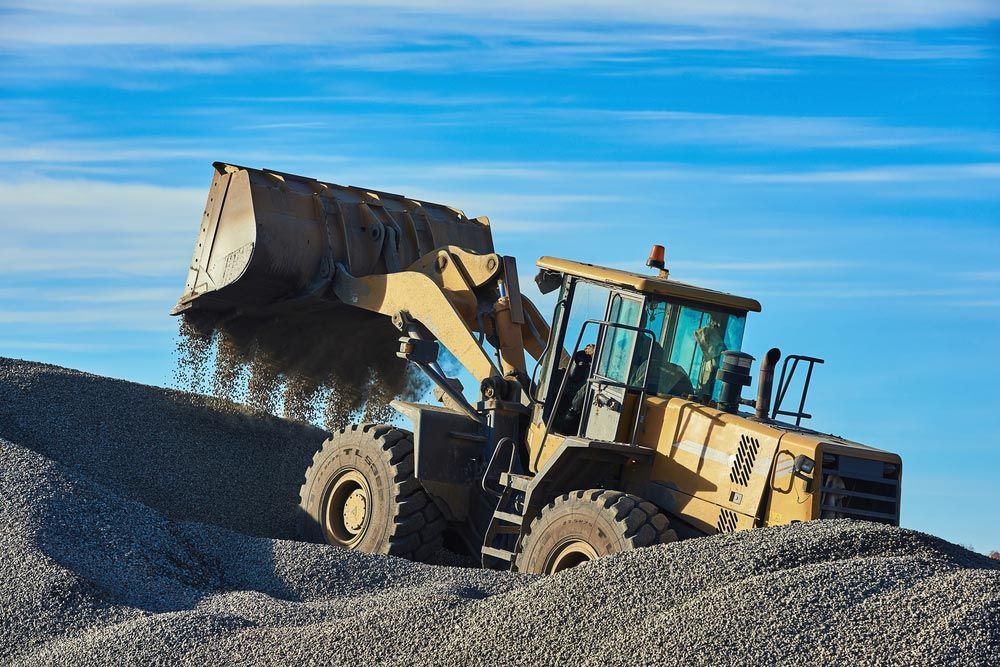 Yellow Loader Dumping Gravel onto A Large Pile Against a Blue Sky — Chooks Sand And Gravel In Proserpine, QLD