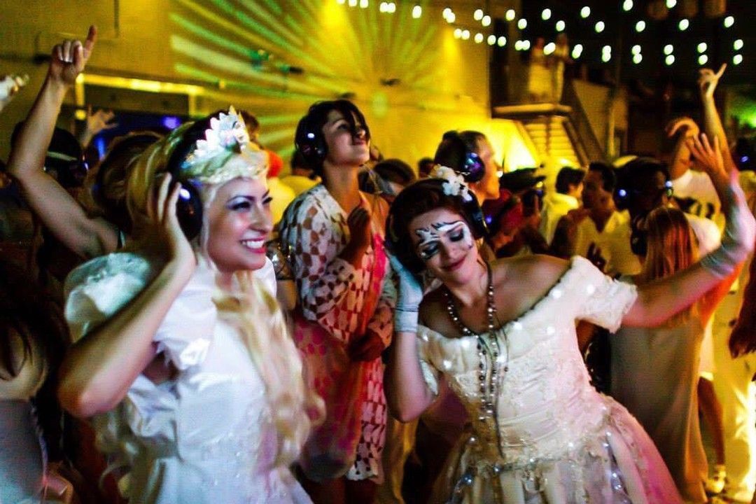 People dancing at a festive party under string lights, wearing colorful costumes and smiling
