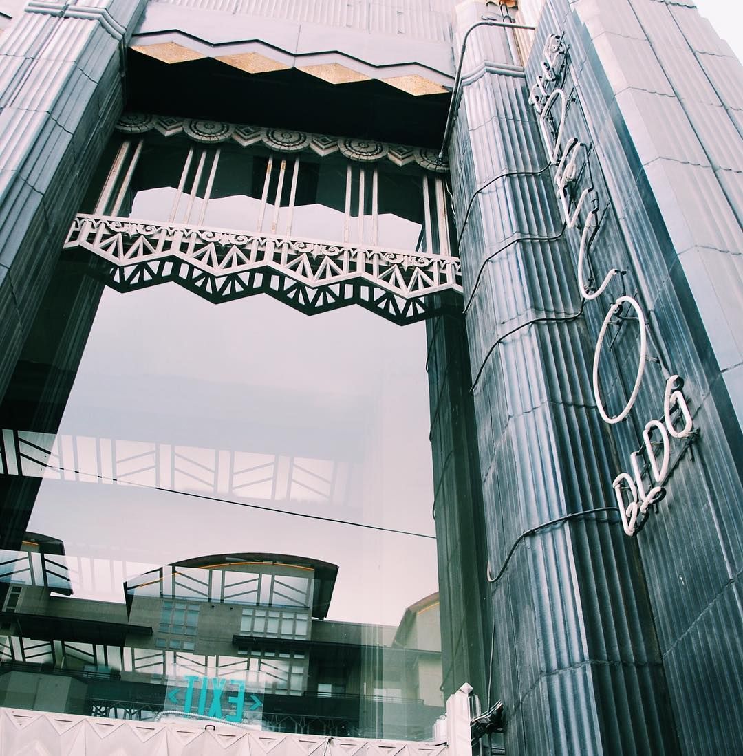 Tall modern glass building entrance with ornate awnings and vertical neon-like lettering on the facade