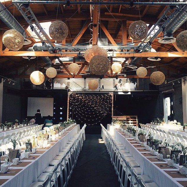 Long banquet tables in a rustic hall with hanging spherical lights and a central aisle.