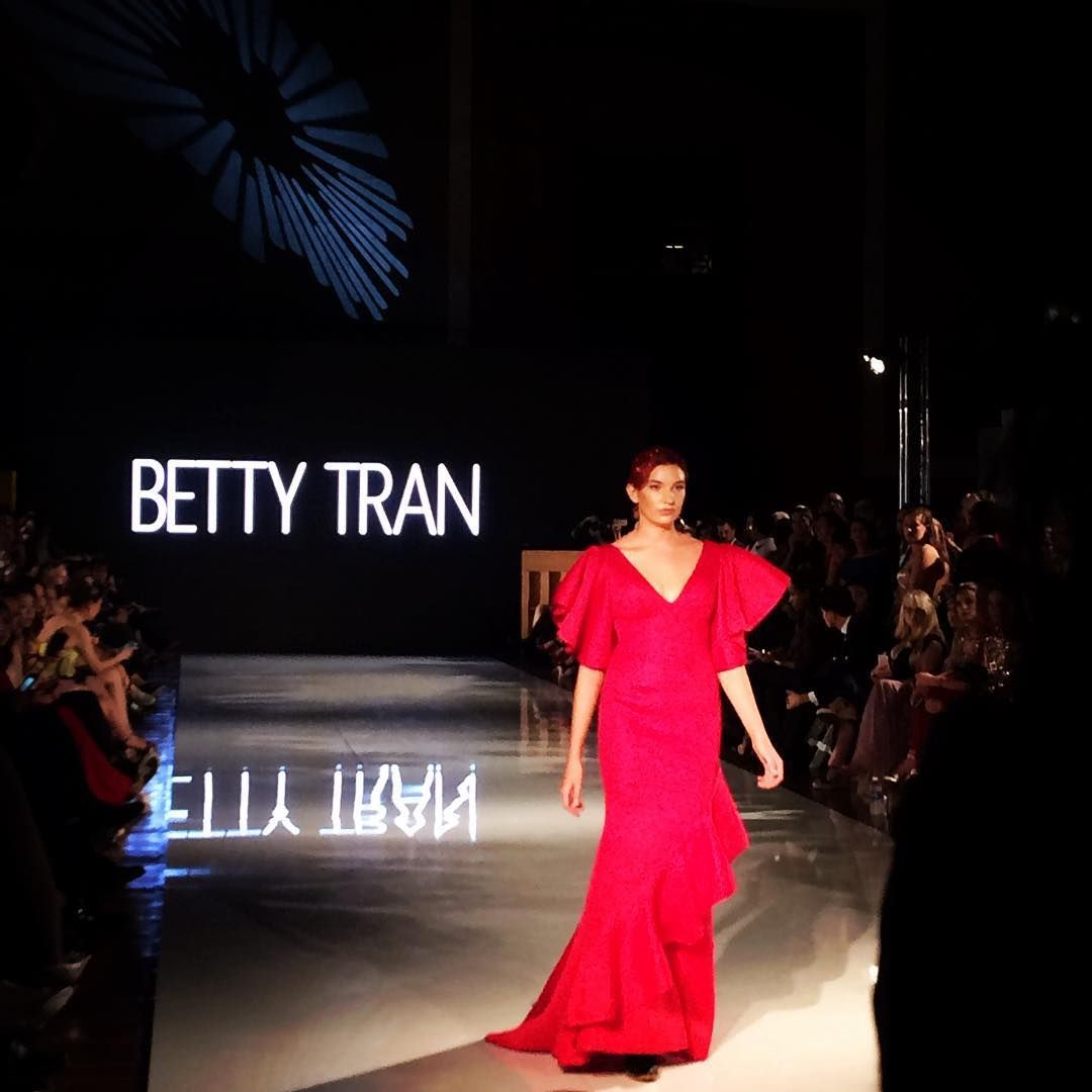 Runway model in bright red gown walking on a BETTY TRAN fashion show catwalk