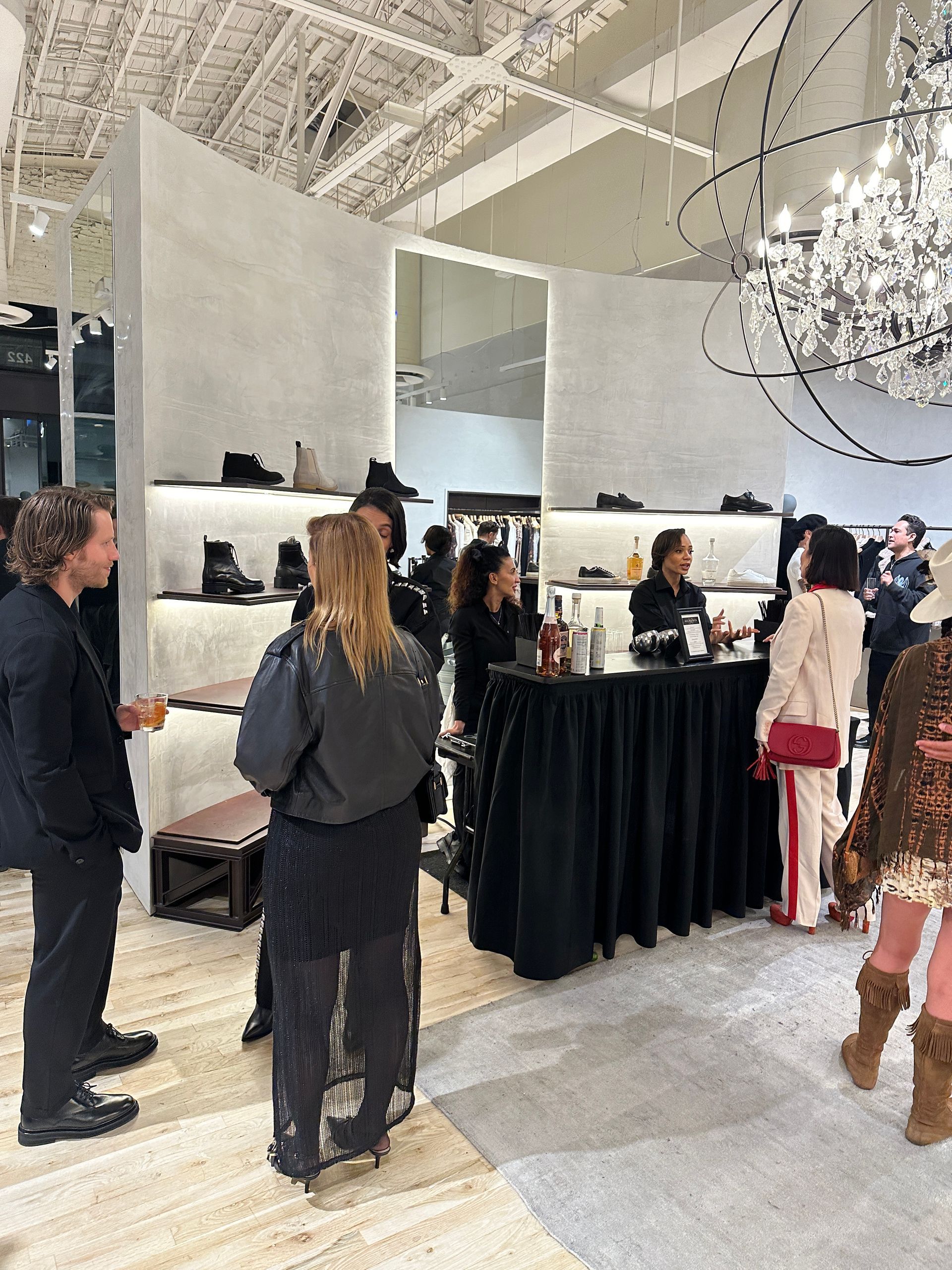 People browsing a fashion display at a bright indoor event with mirrors, racks, and a black-draped counter