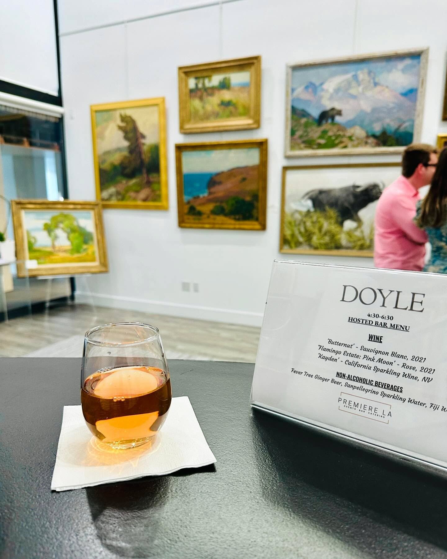 Wine glass on a table with a gallery sign, in an art gallery with framed paintings on the wall.