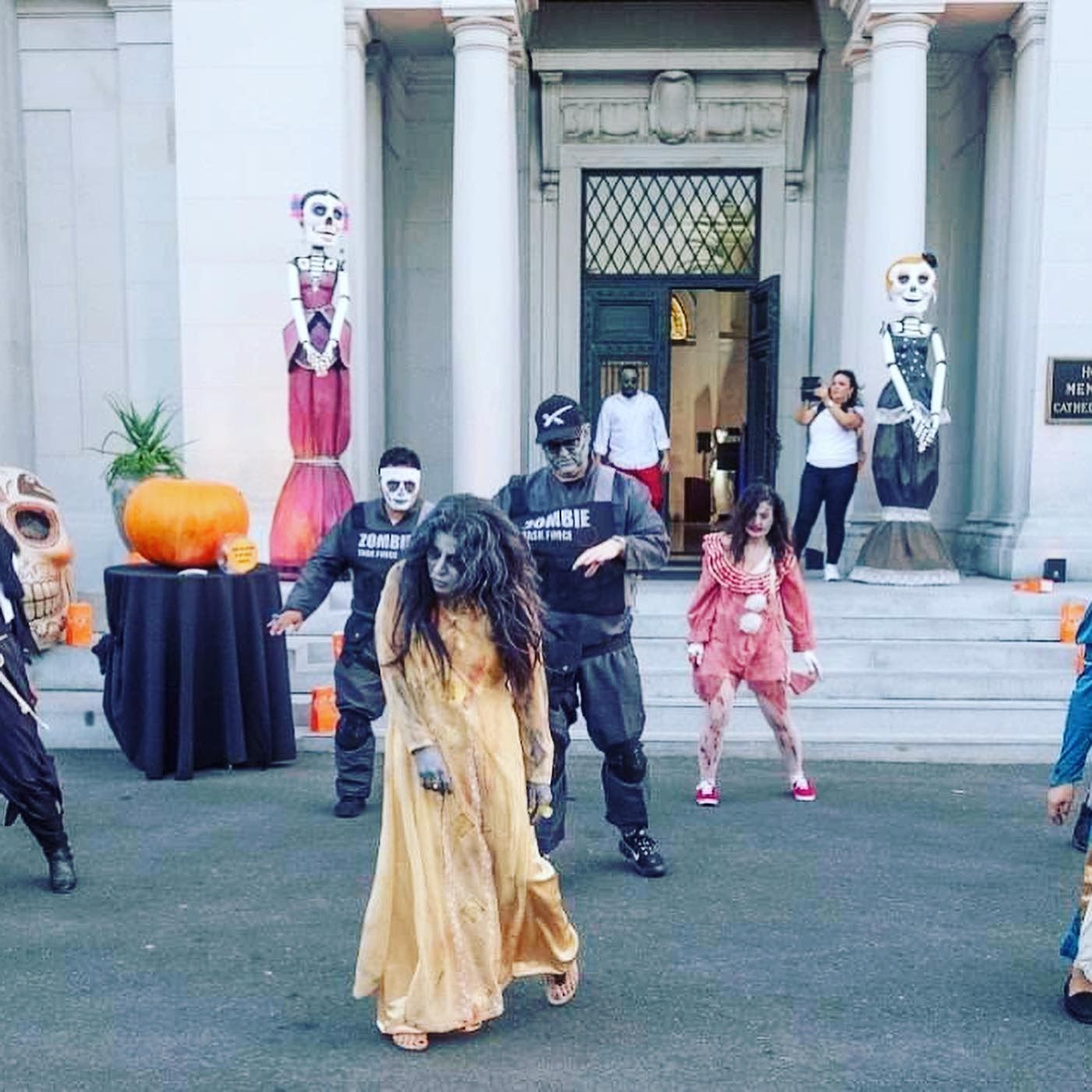 Halloween-costumed people posing on steps outside a grand building with pumpkins and spooky decor