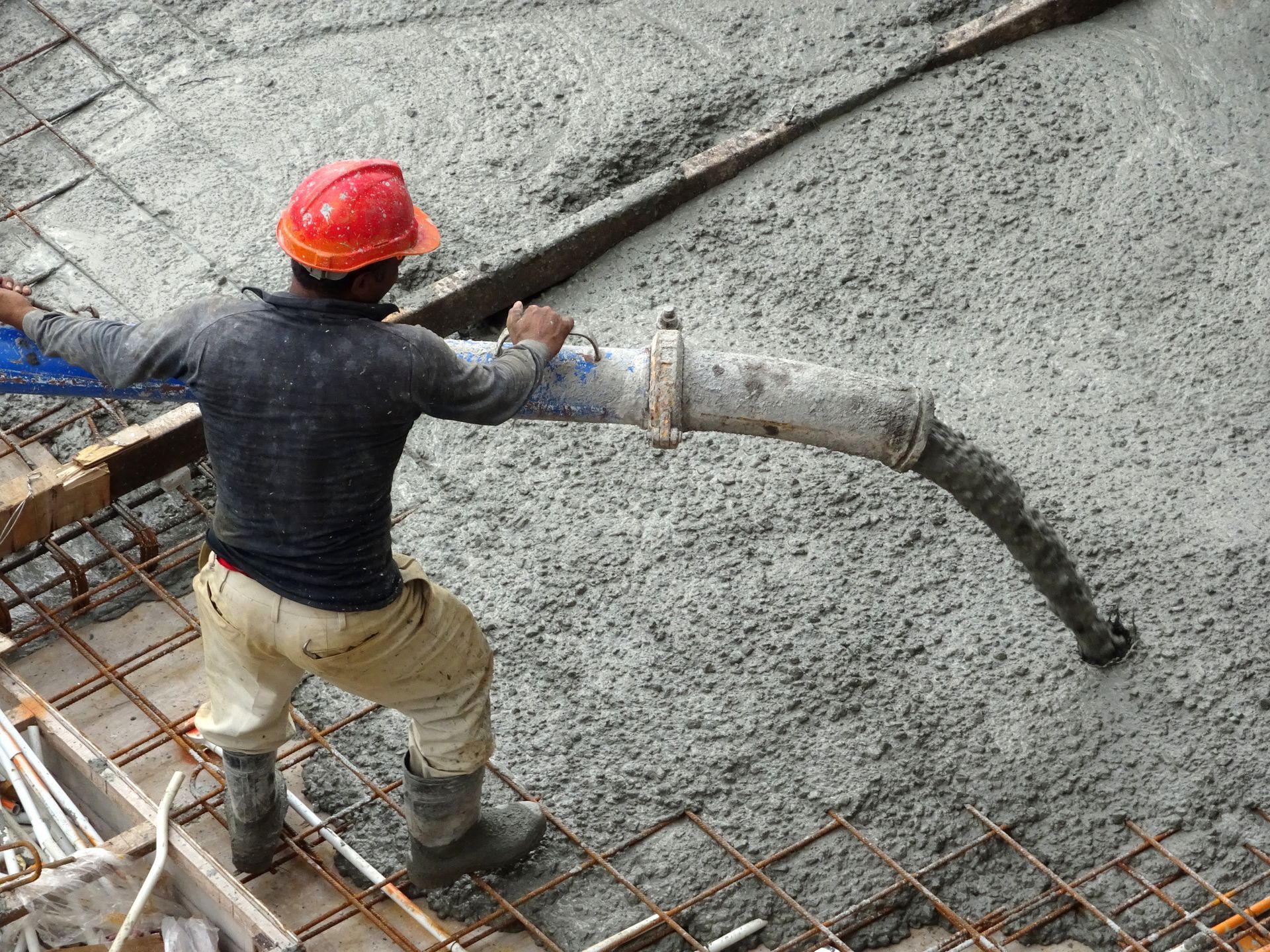 A man is pouring wet concrete using a delivery hose connected to a concrete pump.
