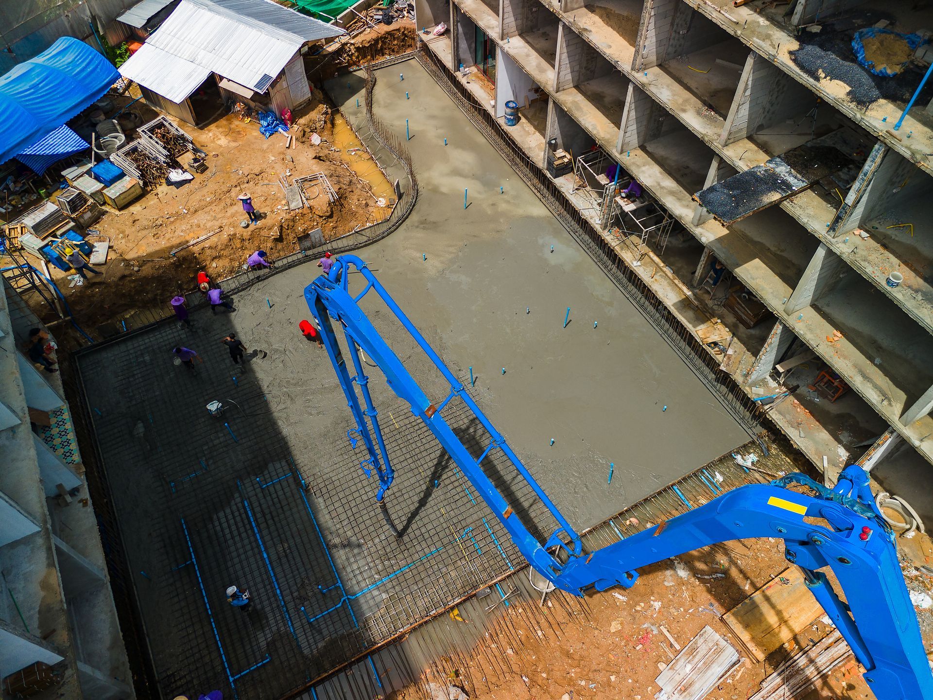 Concrete pump truck pouring foundation as workers guide flow on busy construction site.