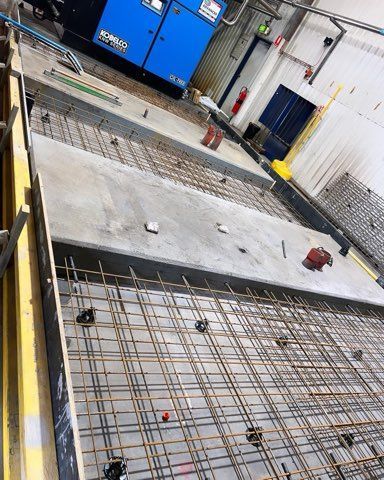 Concrete slab construction: rebar grid, yellow formwork, partial concrete slab, blue generator in a building.