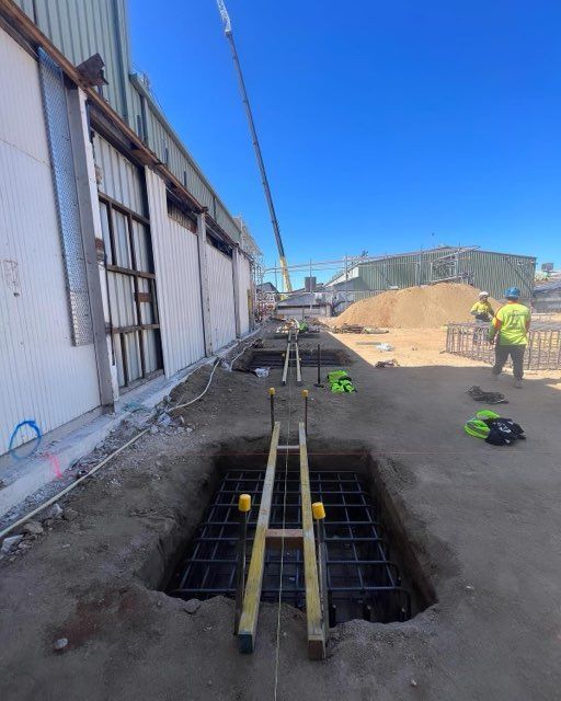 Construction site: Workers preparing a foundation with rebar cages, crane, and building backdrop.