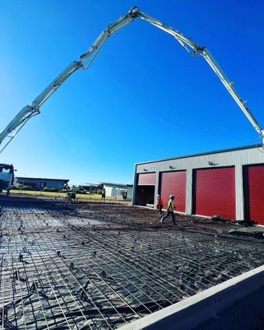 Concrete being poured at a construction site by a boom pump. Workers in safety vests are present. Clear blue sky.