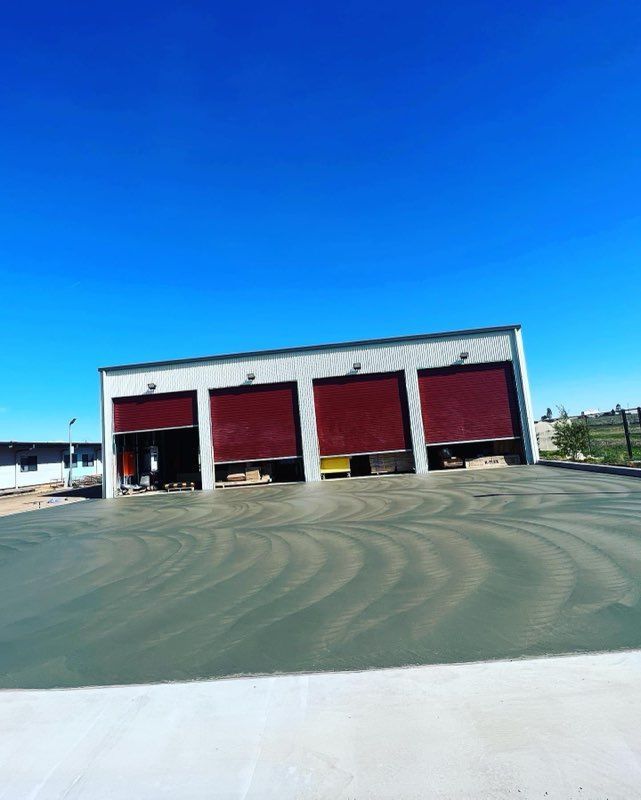 Three bay garage with red doors and wet concrete floor, under a blue sky.