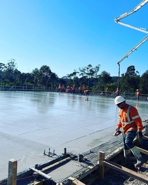 Construction workers pouring concrete on a large flat surface under a blue sky.
