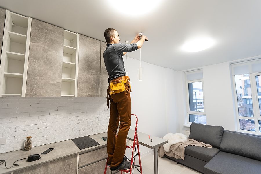 A man is standing on a ladder in a kitchen fixing a light fixture.