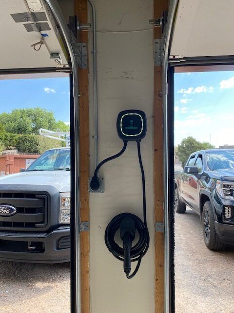 Electric vehicle charging station mounted on a garage wall between two parked trucks.