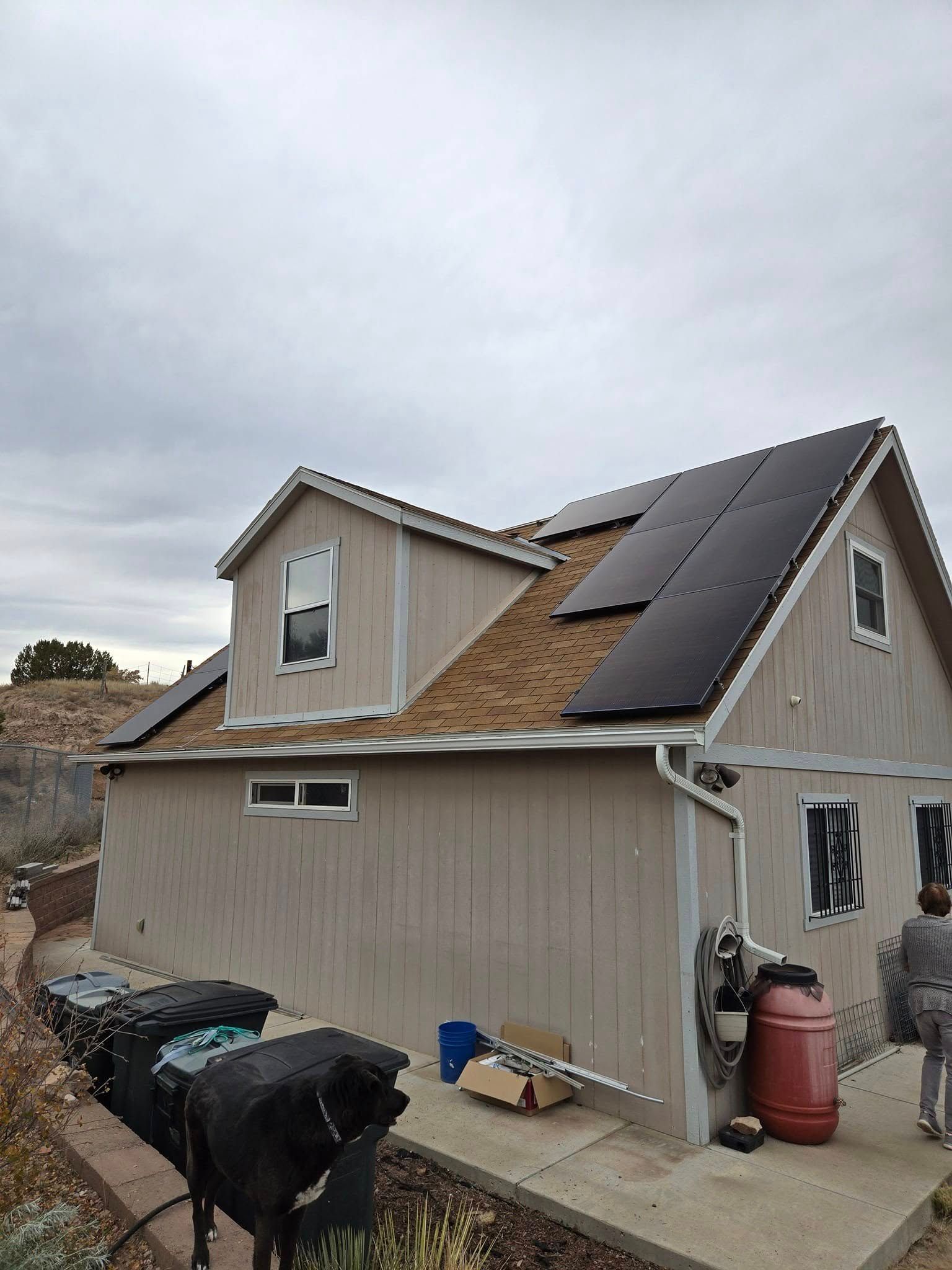 House exterior with solar panels on the roof and trash bins in the driveway