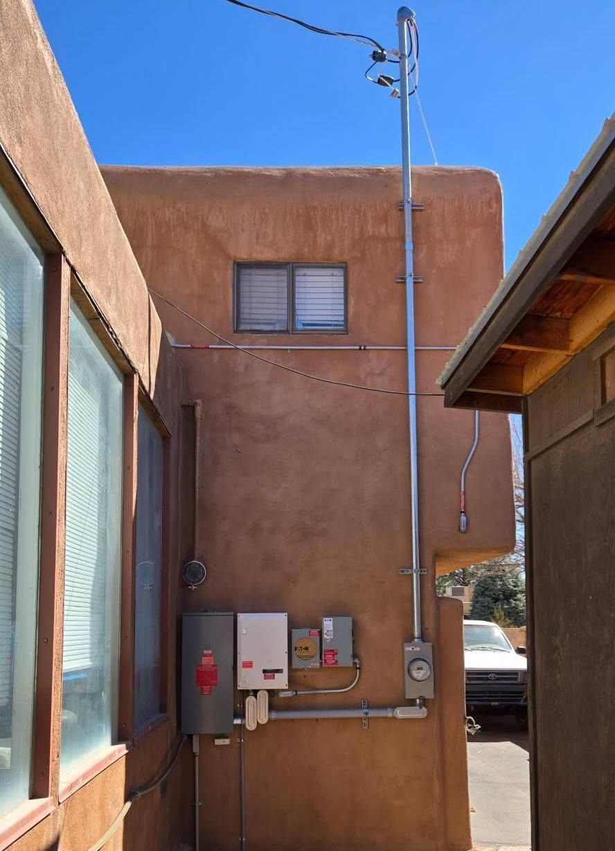 Adobe stucco building with utility boxes and tall antenna between two walls under a blue sky