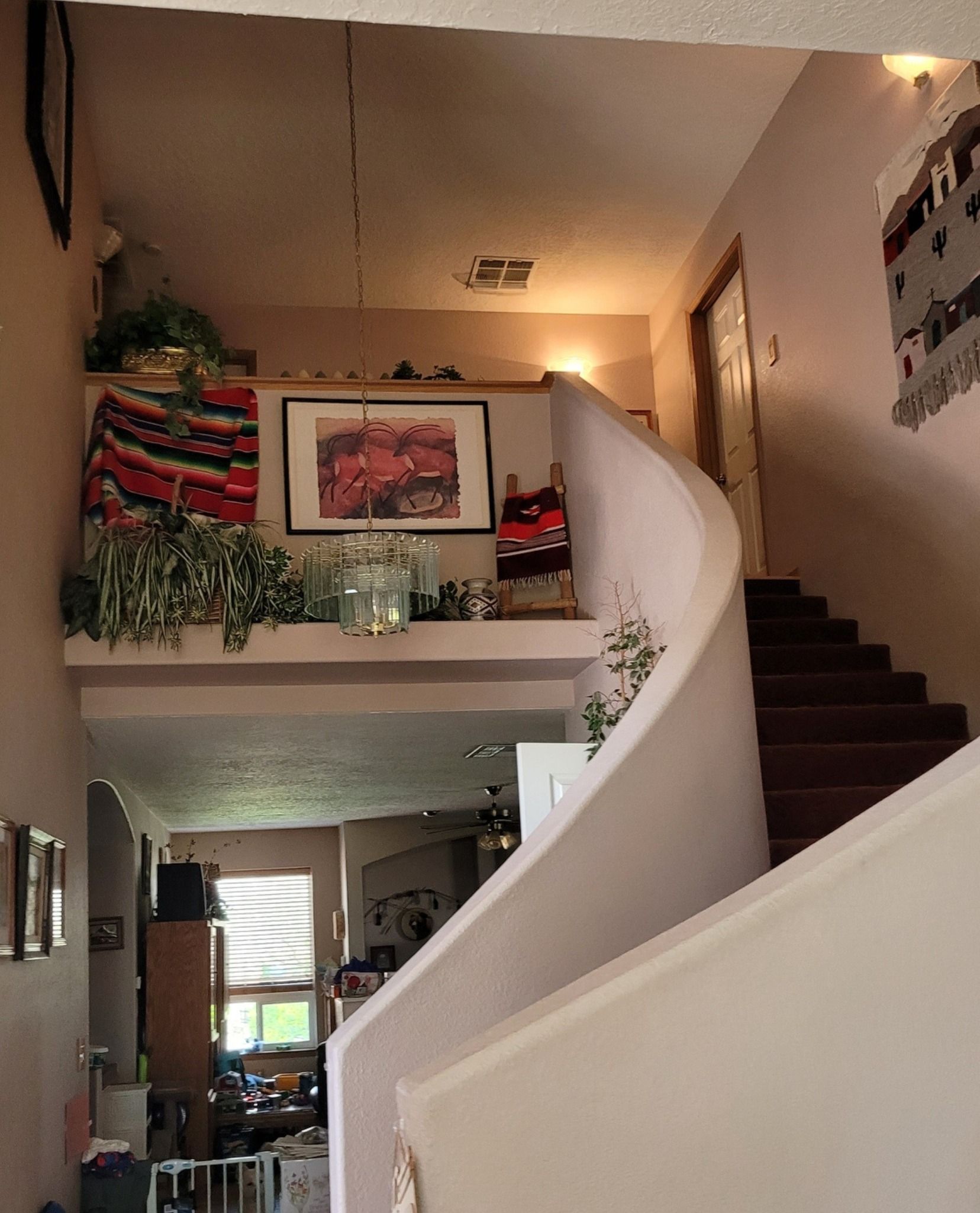 Living room with a curved staircase, loft shelf decor, and plants in a warm indoor home interior