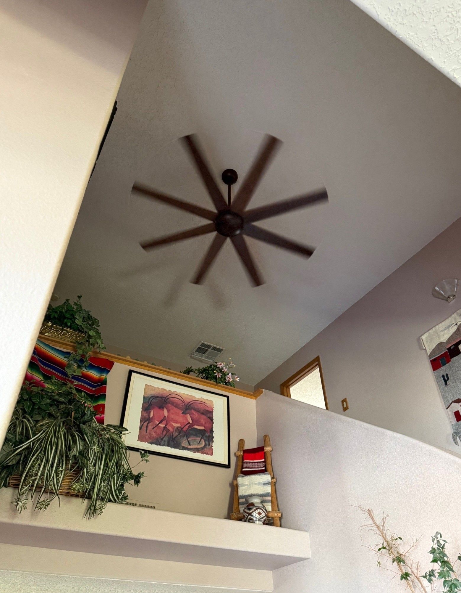 Vaulted living room ceiling with dark wood ceiling fan above a white half-wall and framed artwork.
