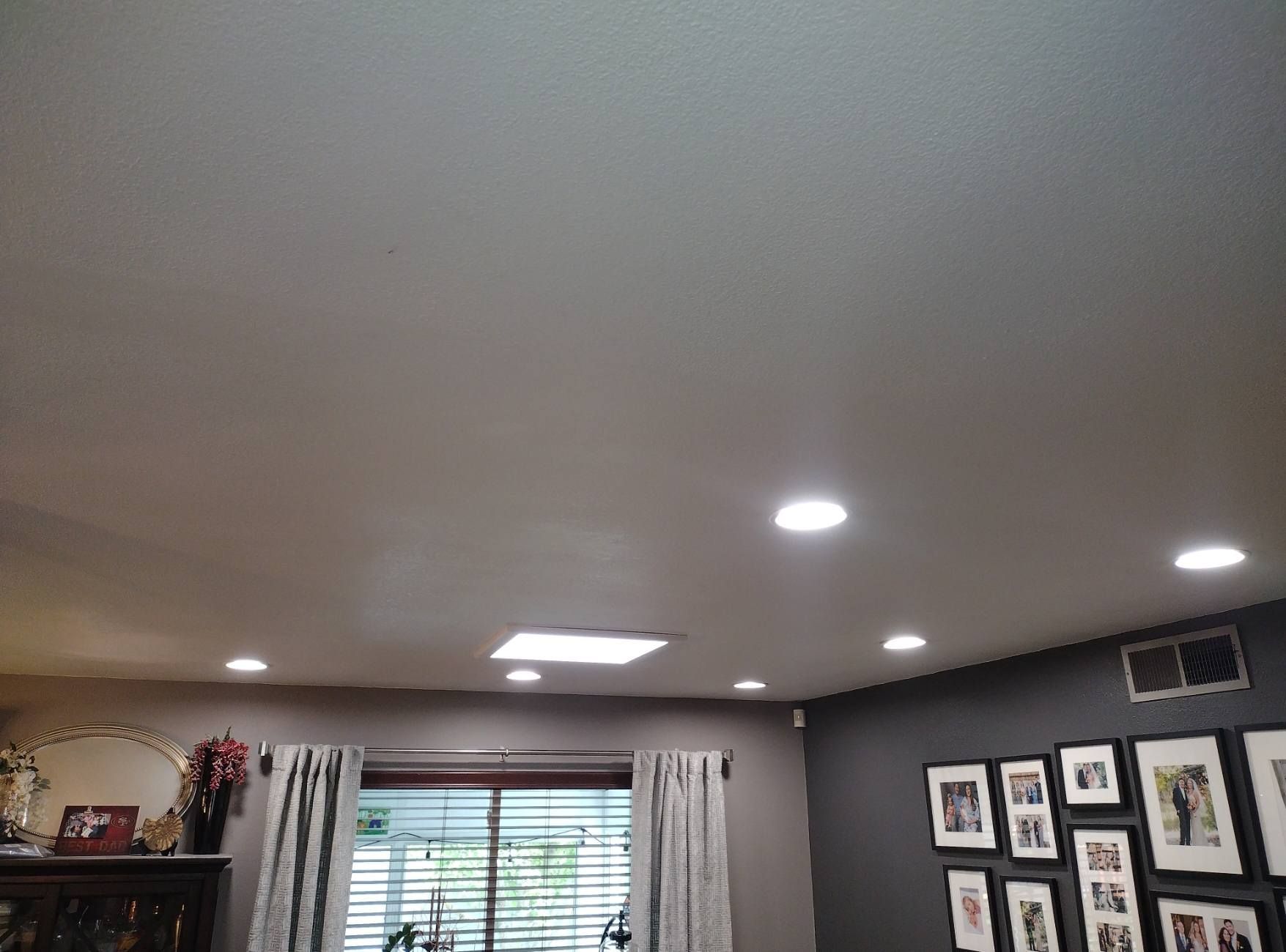 Living room ceiling with recessed lights, a window with curtains, and framed photos on a dark wall