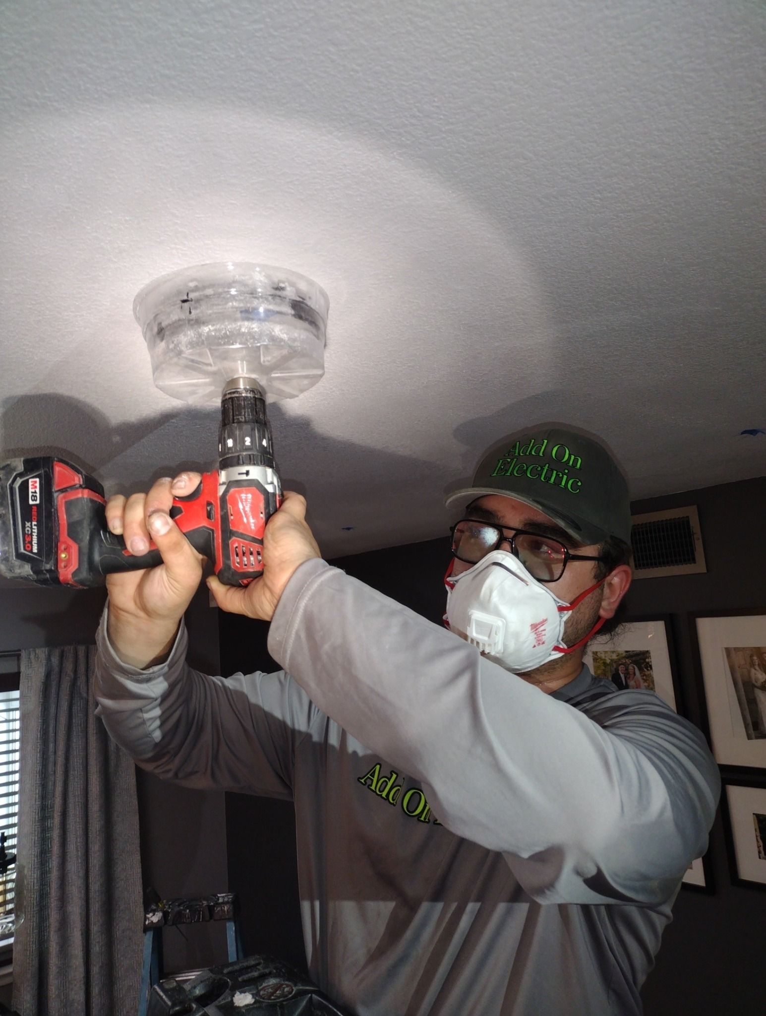 A man wearing a mask is using a drill to install a fire alarm.