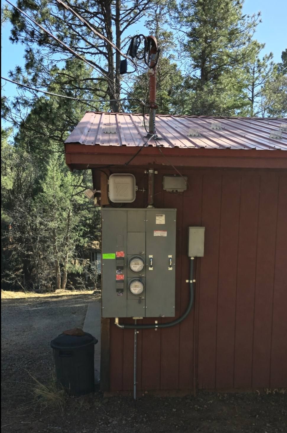 Electrical meter box on a red cabin wall beside a forest clearing