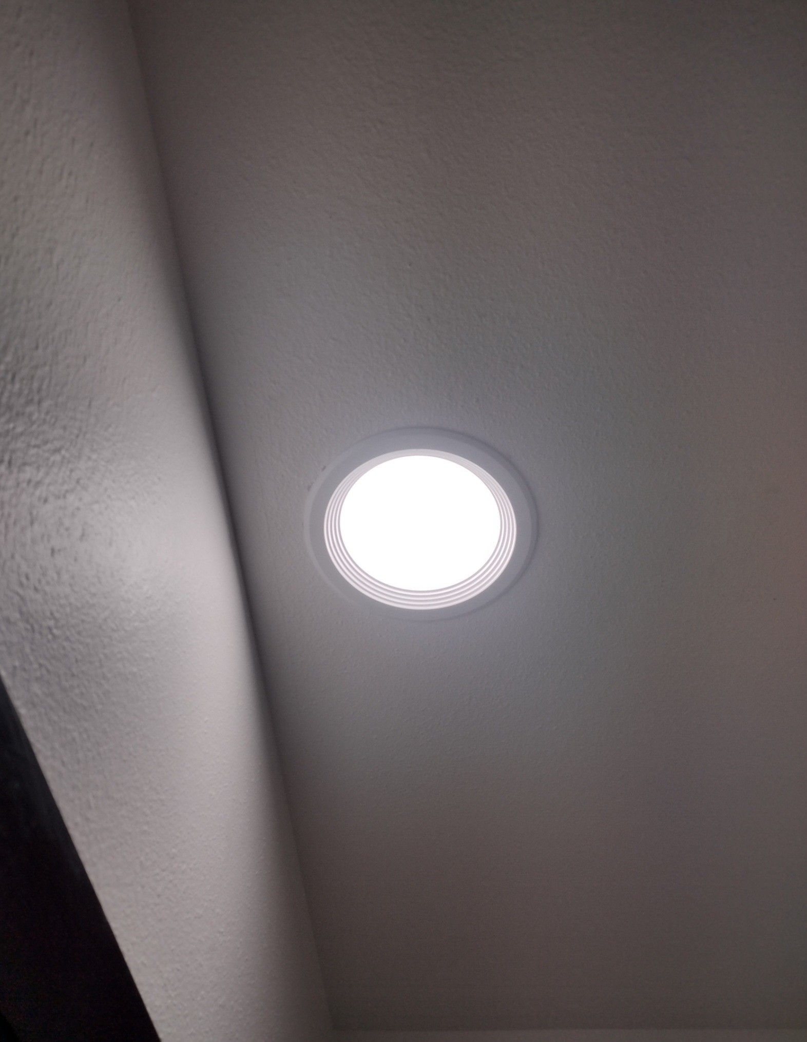 Ceiling with a recessed round LED light in a plain gray room.