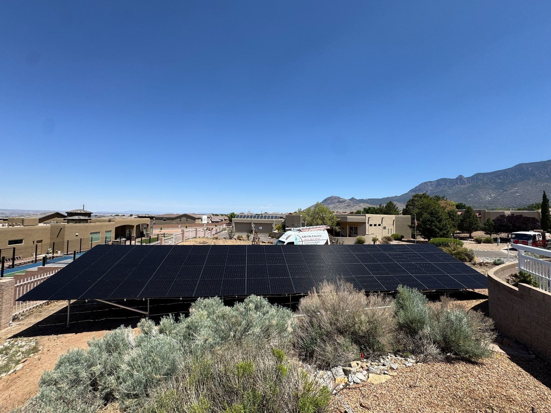 Rooftop solar panels in a desert neighborhood with mountains under a clear blue sky