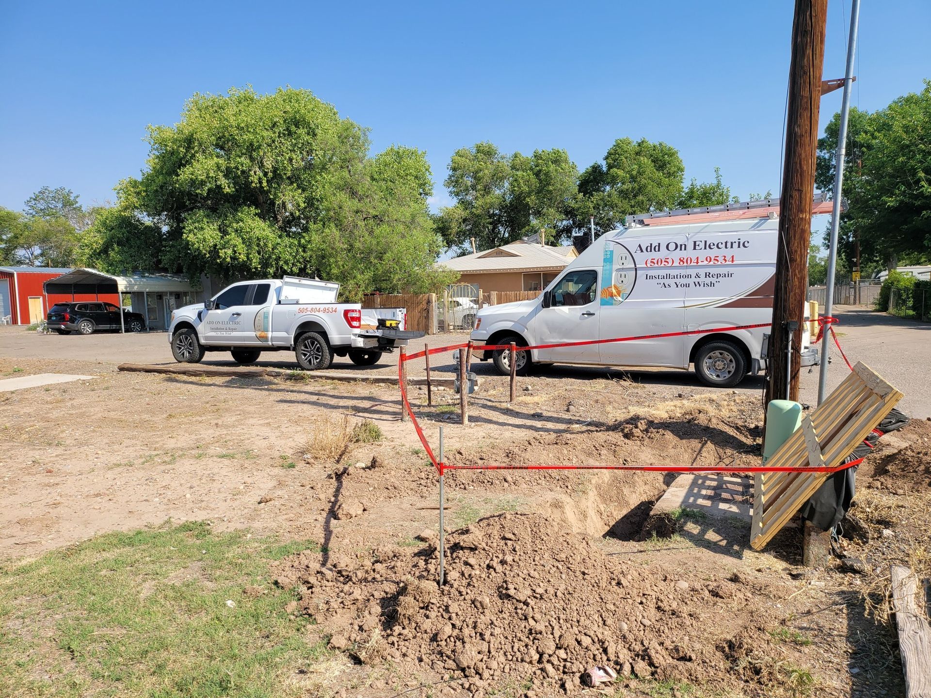 Construction site with truck, van, and orange safety barriers beside a dirt trench