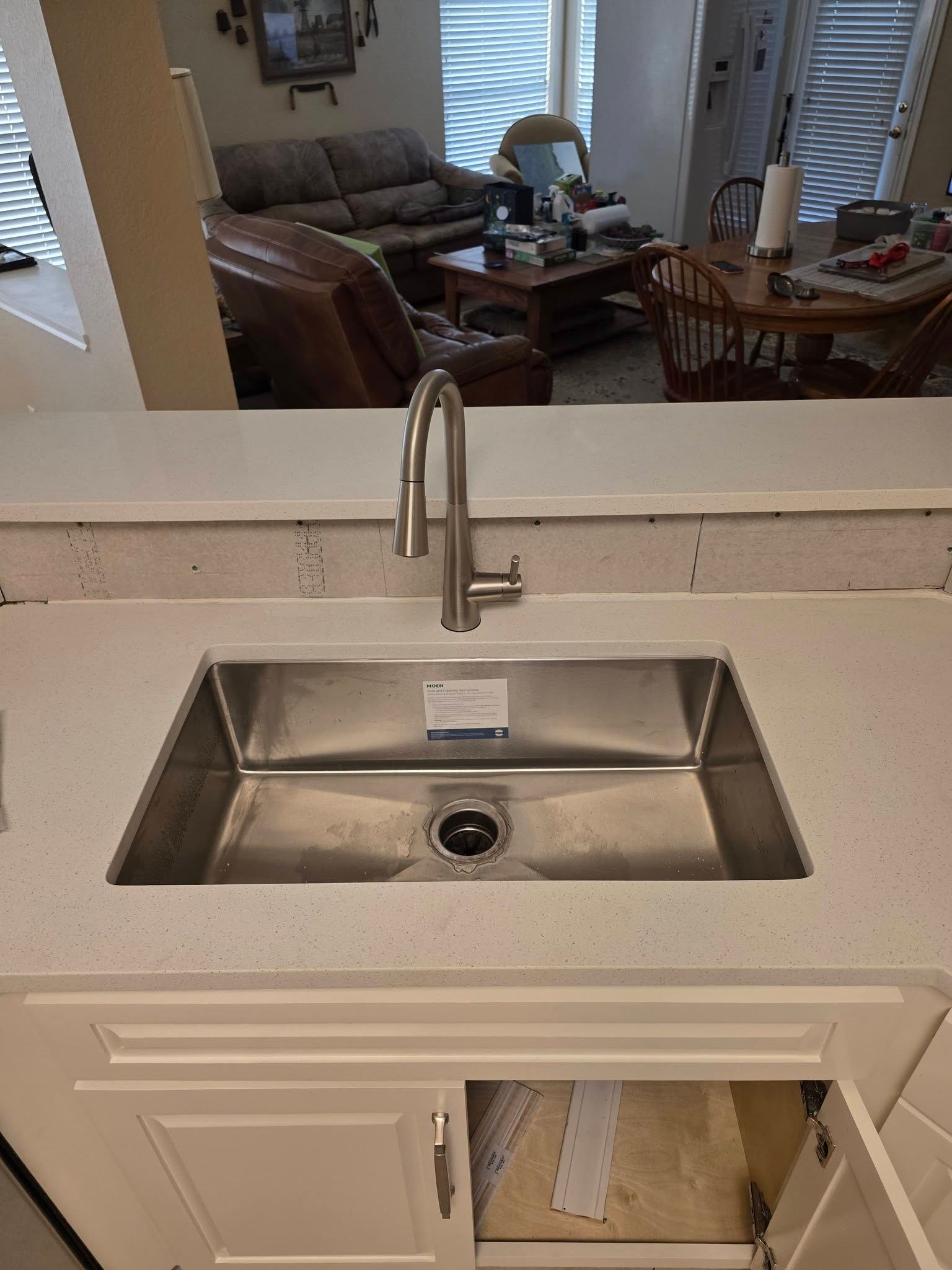 Modern bathroom vanity with rectangular sink, chrome faucet, and a view into the living room beyond.