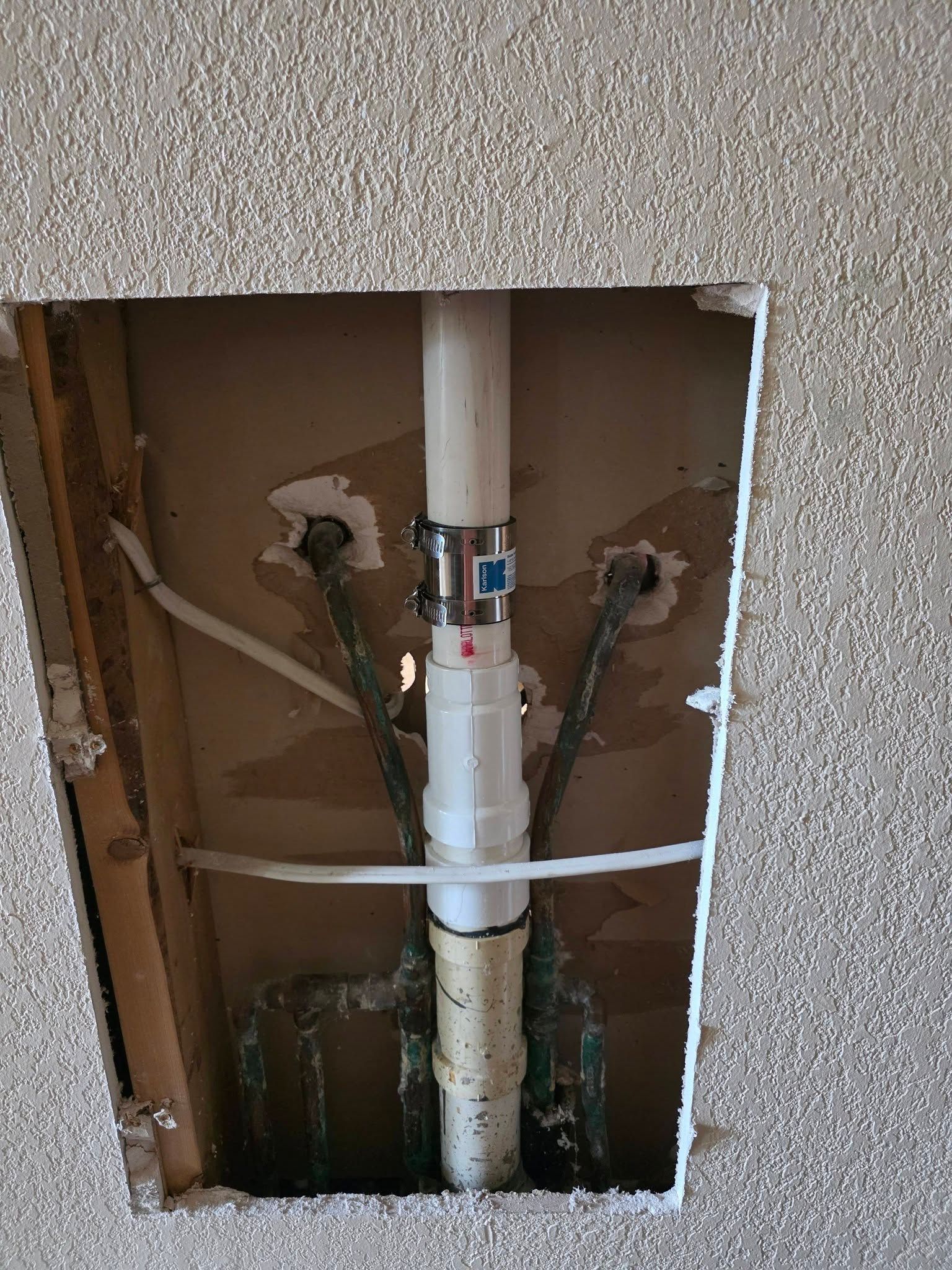 Open wall with exposed white plumbing pipe and fittings, with cut drywall around it