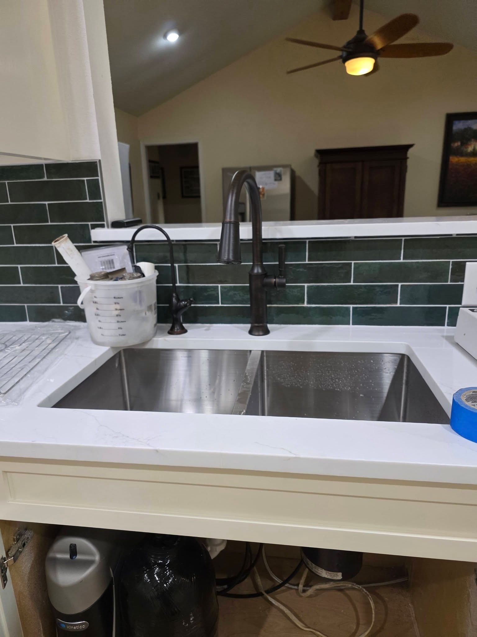 Kitchen sink with matte black faucet, white countertop, and green tile backsplash in a bright room