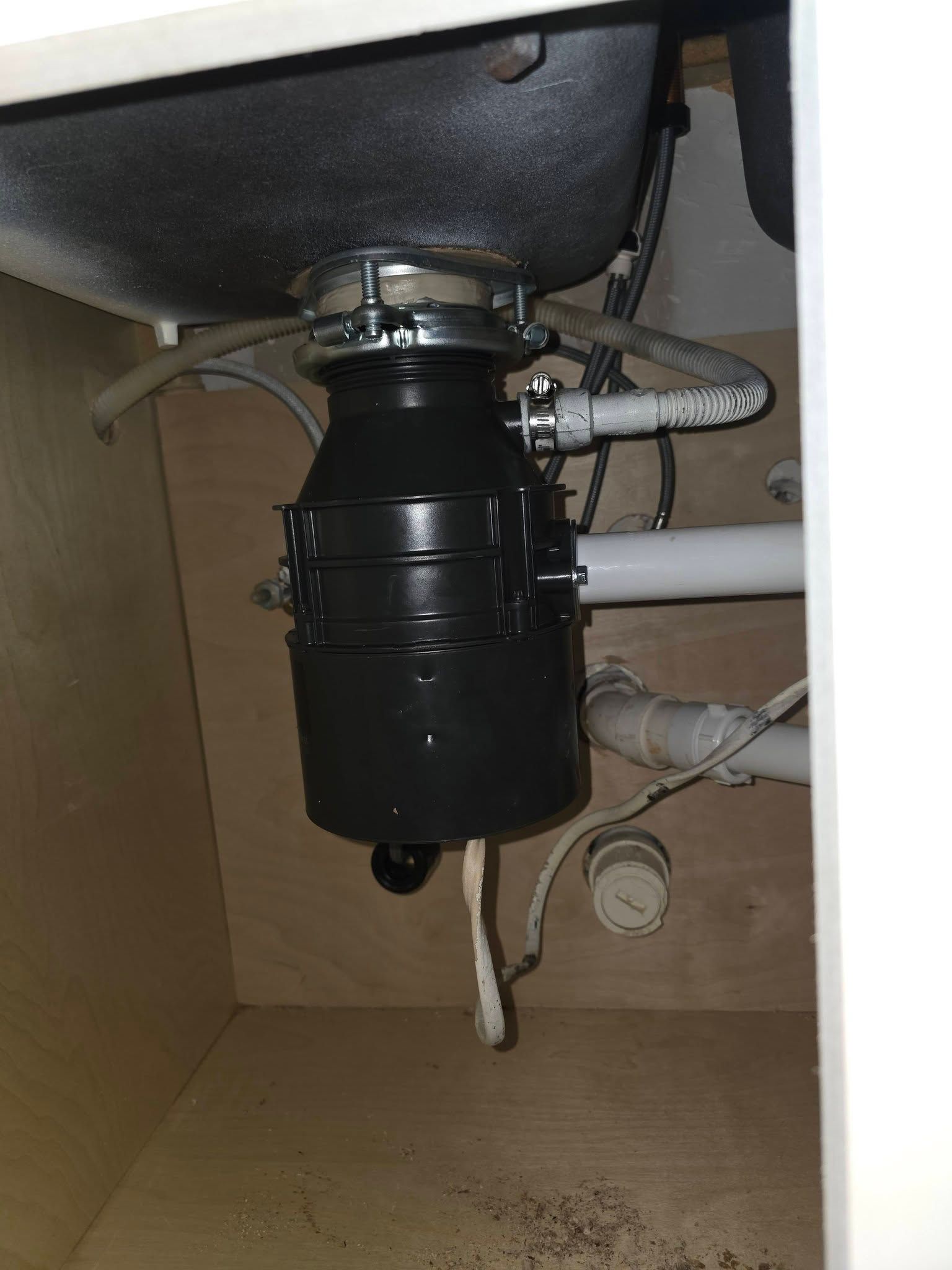 Under-sink garbage disposal and plumbing pipes inside a kitchen cabinet