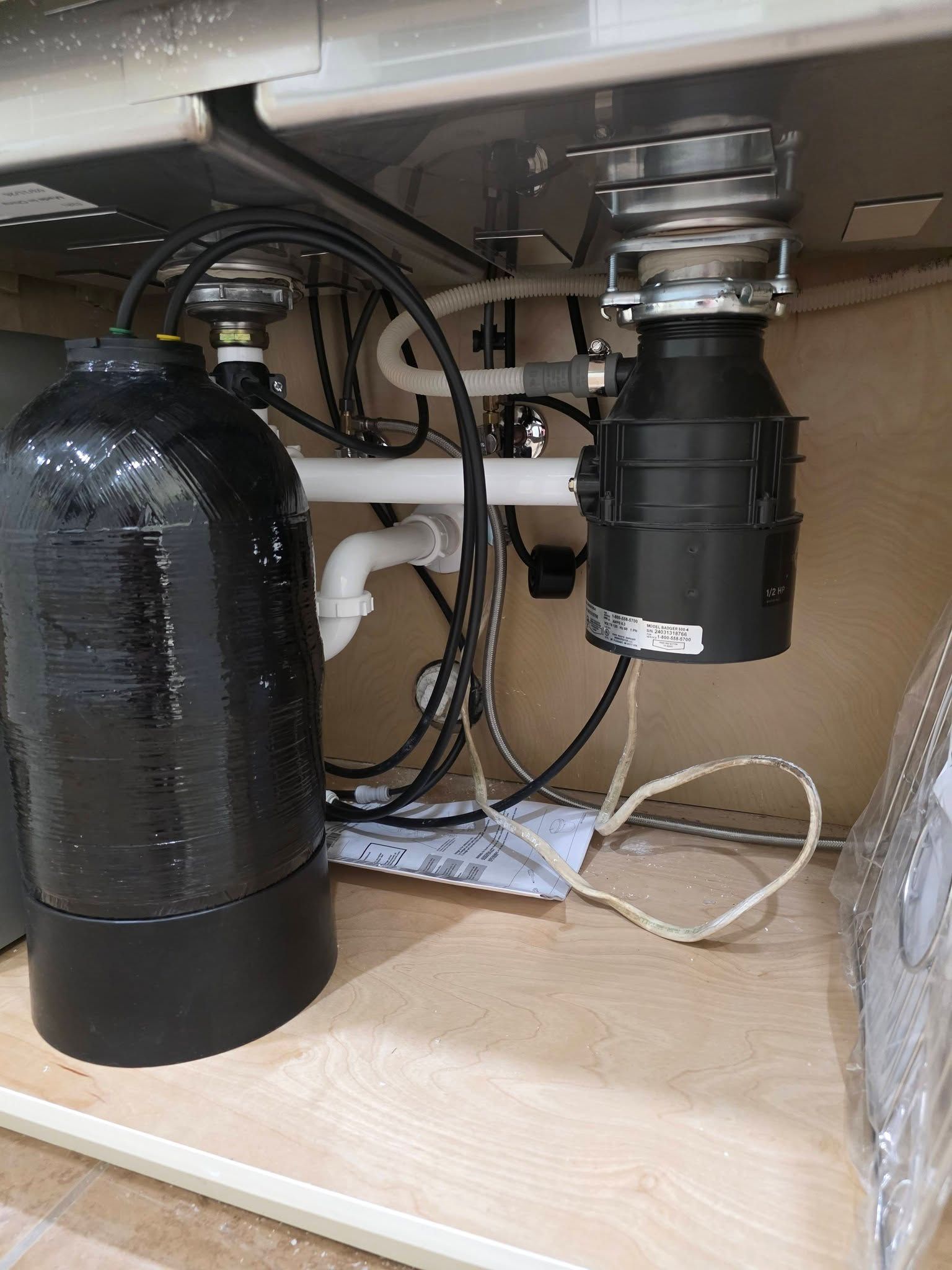 Under-sink plumbing and disposal with black tank, pipes, and cords in a cabinet
